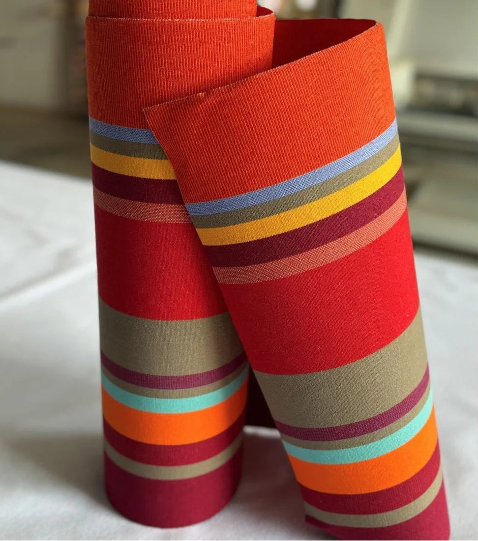 Close up of Collioure Rouge - a fabric featuring a striped pattern with various bands in reds, orange, taupe, burgundy, turquoise, and other vibrant colours. A detailed 100% cotton weave by By Les Toiles du Soleil