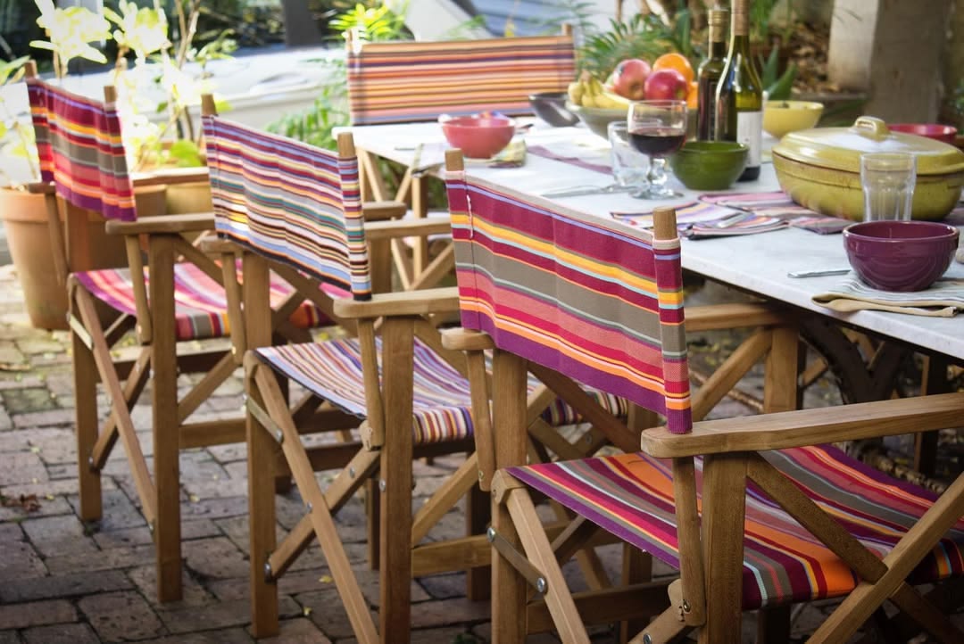 Outdoor dining setup with striped Les Toiles du Soleil and Sunbrella director chairs and a table set for a meal.