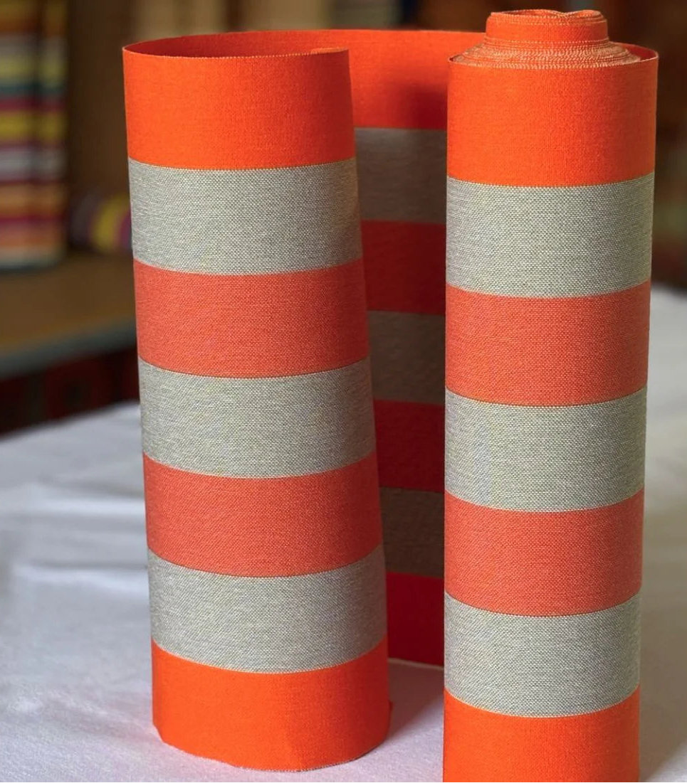 Close up of Carthage Tomette Orange fabric roll featuring a bold stripes of red, orange red, and beige/brown. A detailed 100% cotton weave by By Les Toiles du Soleil