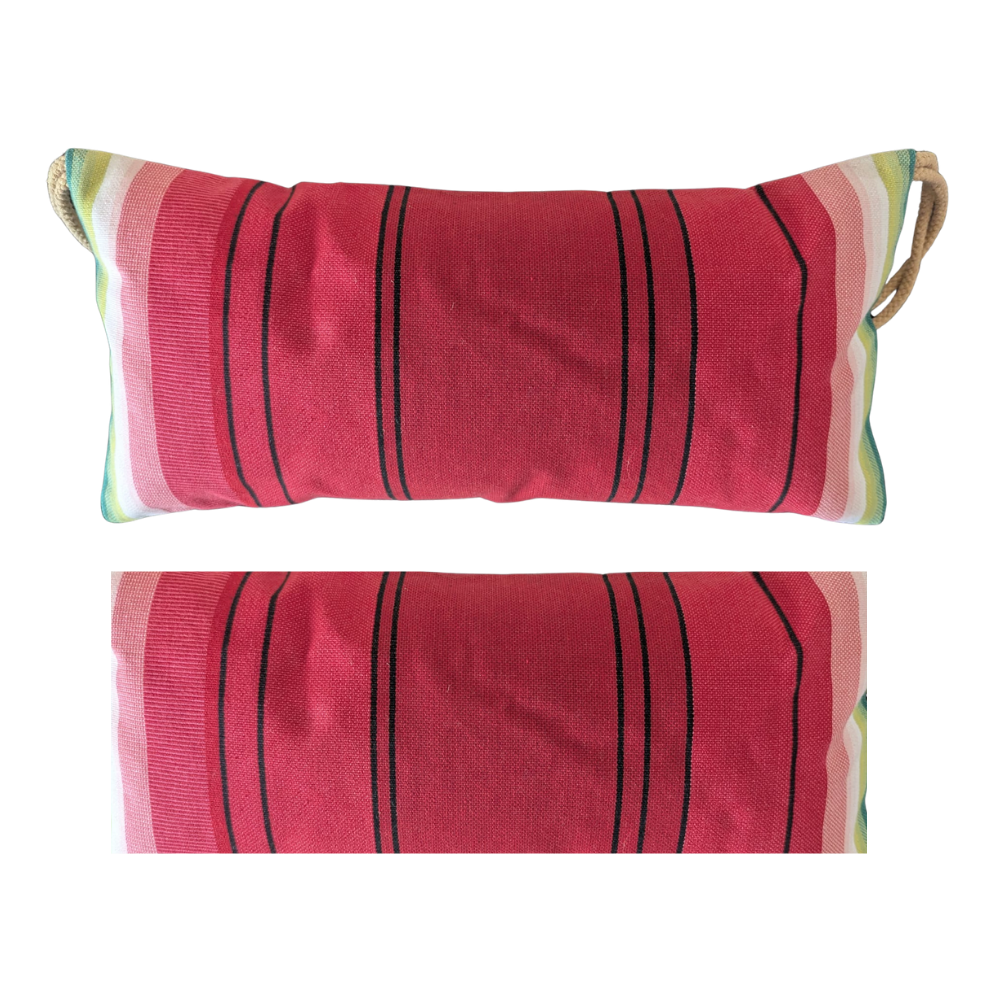 A rectangular lumbar pillow with a woven red-pink body, black vertical stripes, and a striped border in green, cream, and pink, featuring natural jute rope handles on the sides, shown against a plain white background.