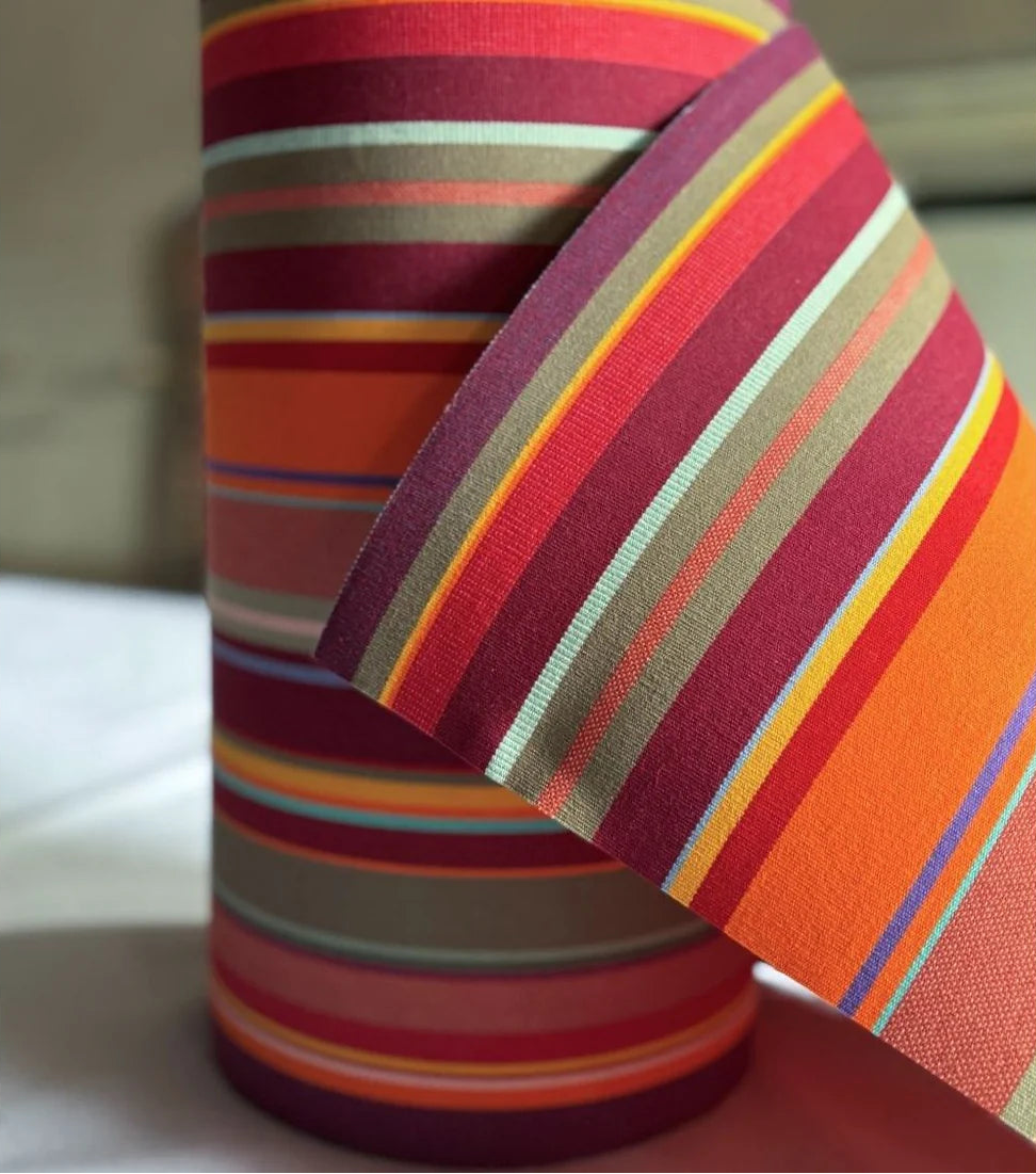 Close up of 43cm cotton Fabric in St Vincent Rouge, featuring a multicoloured striped pattern with various bands in reds, orange, purple, browns and different colours, indicating a vibrant and lively design. By Les Toiles du Soleil
