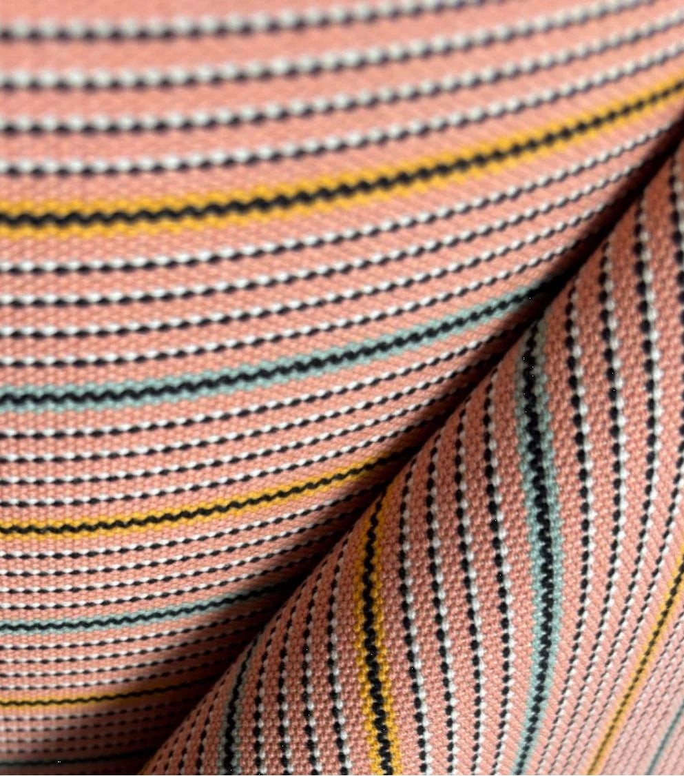 Close-up of the 1897 No.1 fabric roll showing woven vertical stripes in soft pink, red, beige, and cream tones with a textured linen-cotton weave. Made by Les Toiles du Soleil