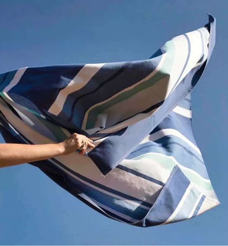 Someone flapping in the sky blue air Aigue Marine fabric, which is a multi coloured striped fabric made by Les toiles du Soleil. It showcases a variety of shades of blue