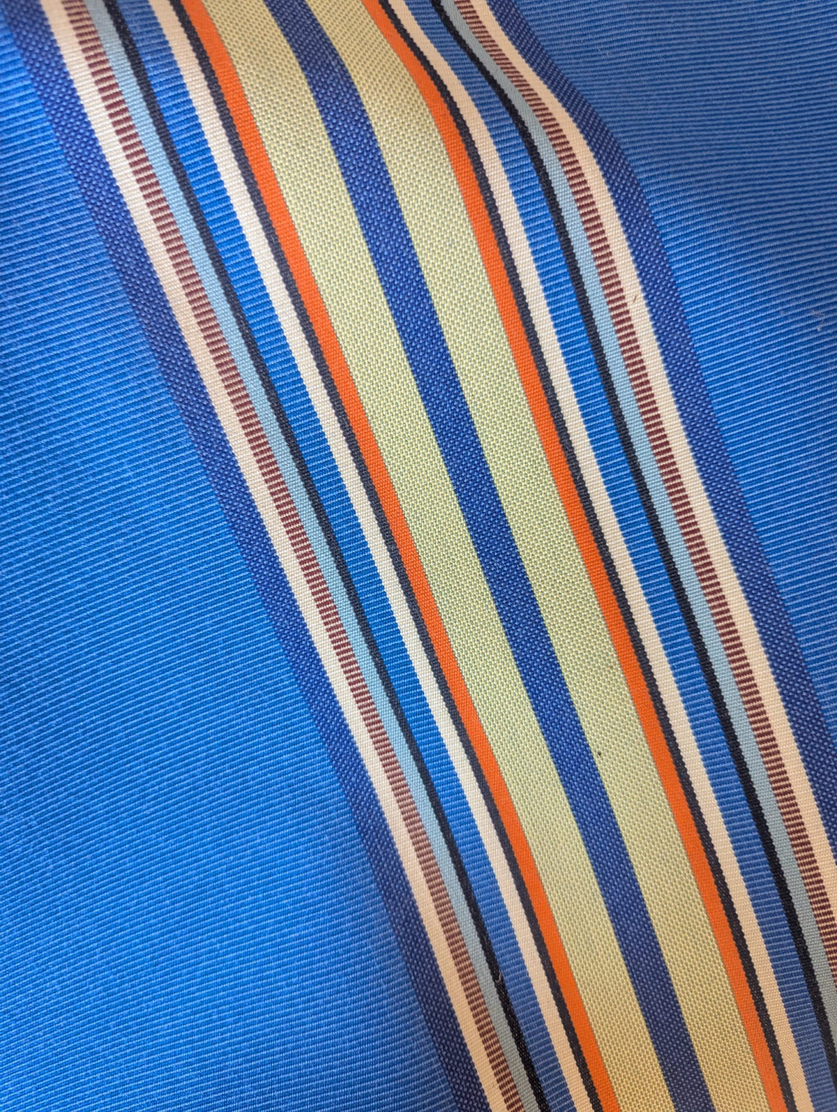 close up of  outdoor Sunbrella and Les Toiles du Soleil fabric. Showing multi-coloured stripes of blues, beige, green, orange and red.
