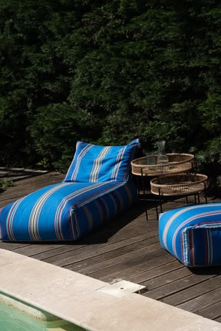 Les Toiles do Soleil outdoor fabric Alexandra Blue striped outdoor lounge chairs on a wooden deck with trees in the background
