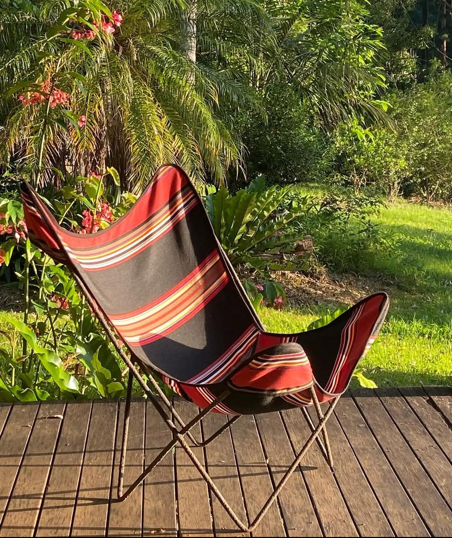 Jules Les Toiles du Soleil Sunbrella outdoor striped fabric on chair on a wooden deck with a lush green garden background