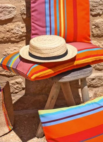 Bonbon plume colorful Sunbrella and Les Toiles du Soliel striped cushions with a straw hat on a stone surface