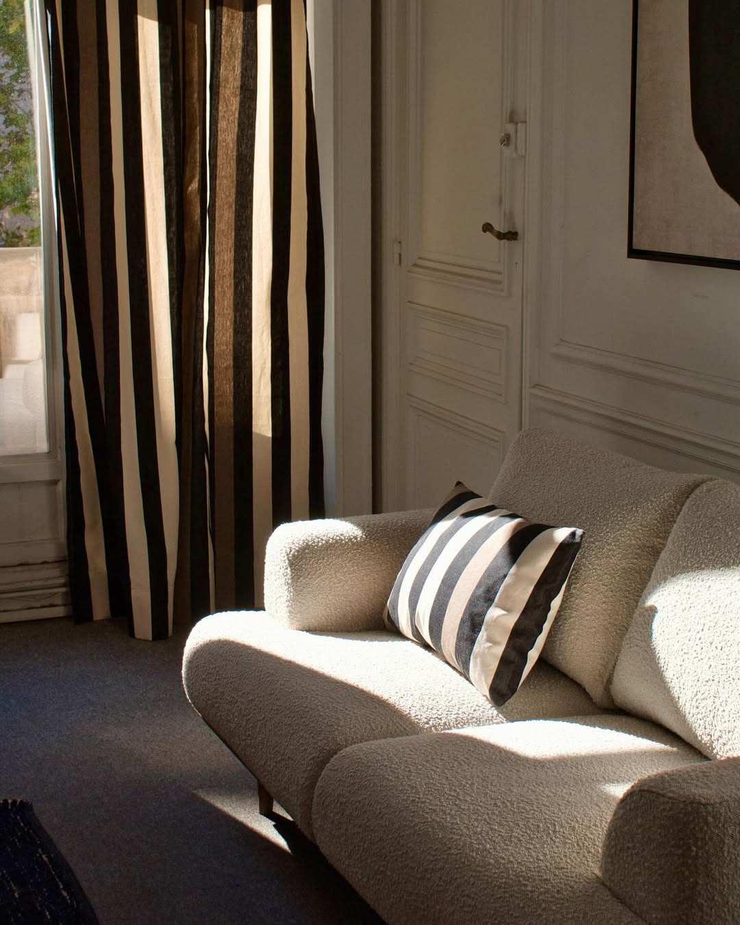 Light coloured Living room with curtains and a cushion on a soft cream couch made from Boulevard Raspail Taupe 100% cotton Les Toiles du Soleil 180cm with black, brown and neutral multi striped fabric