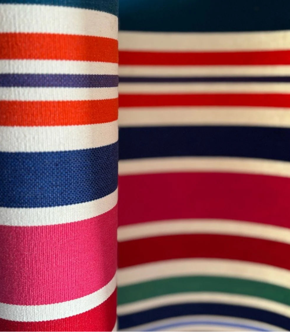 Close up of cotton roll featuring bold stripes of navy, red, fuchsia, orange, teal, green, cream and purple, with a fine orange selvedge edge.