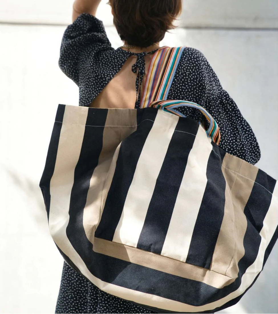 Person carrying a large shoulder tote bag featuring bold black, ecru stripes in-between taupe coloured stripes on the edges