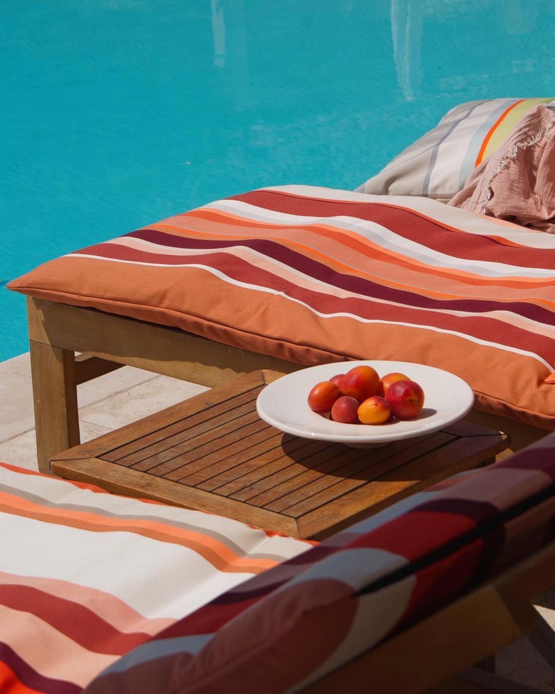 Pool side setting with sun lounge mattresses made from  Cayrou Les Toiles du Soleil Sunbrella outdoor fabric. Multi coloured striped fabric with shades of terracotta and warm tones