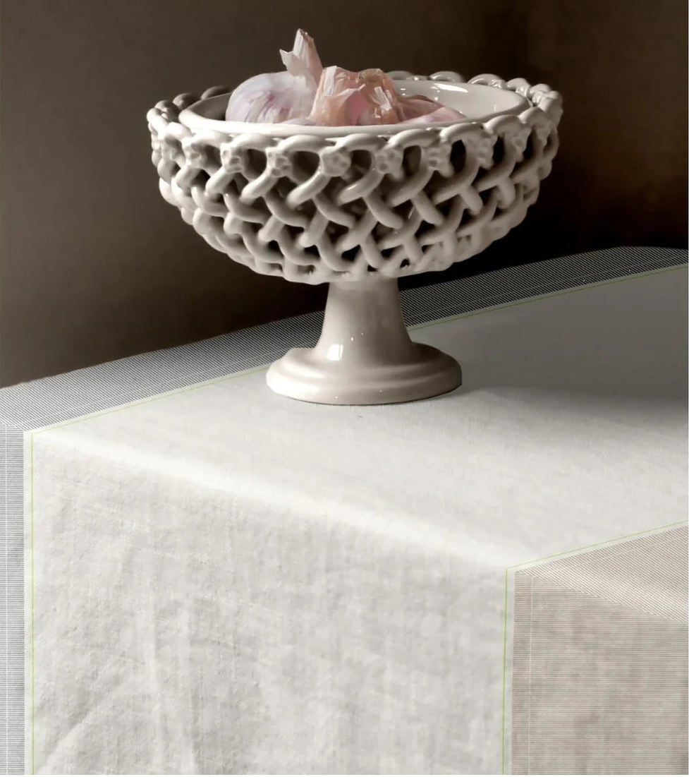 Decorative ceramic bowl with intricate lattice design on a pedestal, containing decorative items, on a  Les Toiles du Soleil 100% Charlotte Bronze fabric with a checkered pattern and blue stitching detail Tablecloth