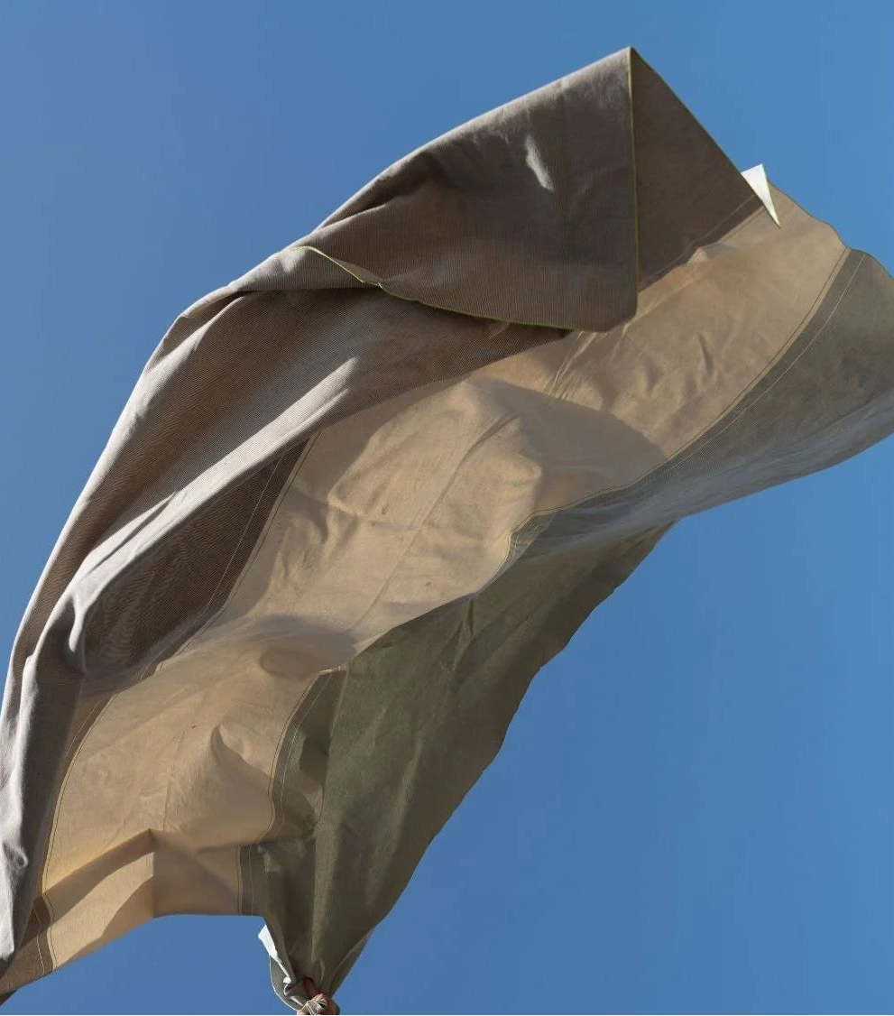 Les Toiles du Soleil Charlotte Bronze cotton fabric thrown in the air with a sly blue background
