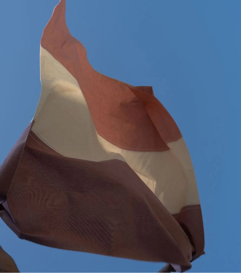 Les Toiles du Soleil Charlotte Tomette fabric of sweet terracotta, lavender blue and cream stripes 100% cotton fabric lifestyle shot of a person throwing it in the air, with a sky blue background