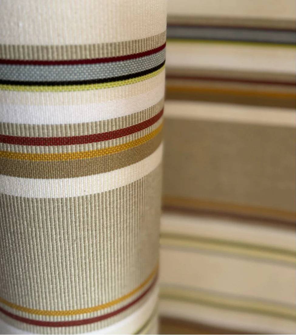 Close up of striped cotton fabric roll featuring soft browns, beige, white, blue and yellows. 