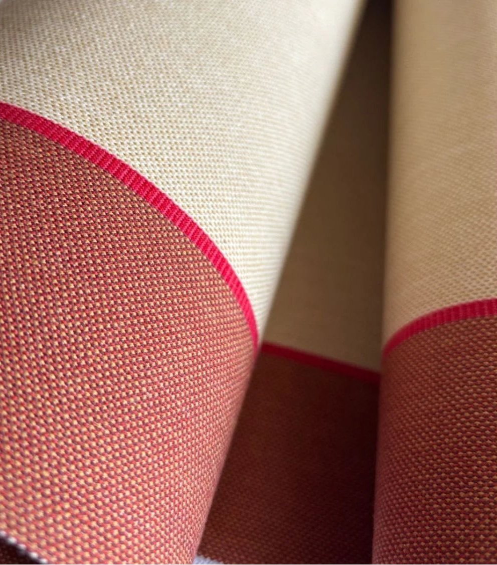 Close-up of a rolled cotton fabric featuring a wide warm écru centre stripe flanked by broad terracotta bands, with a fine crimson accent line between them.