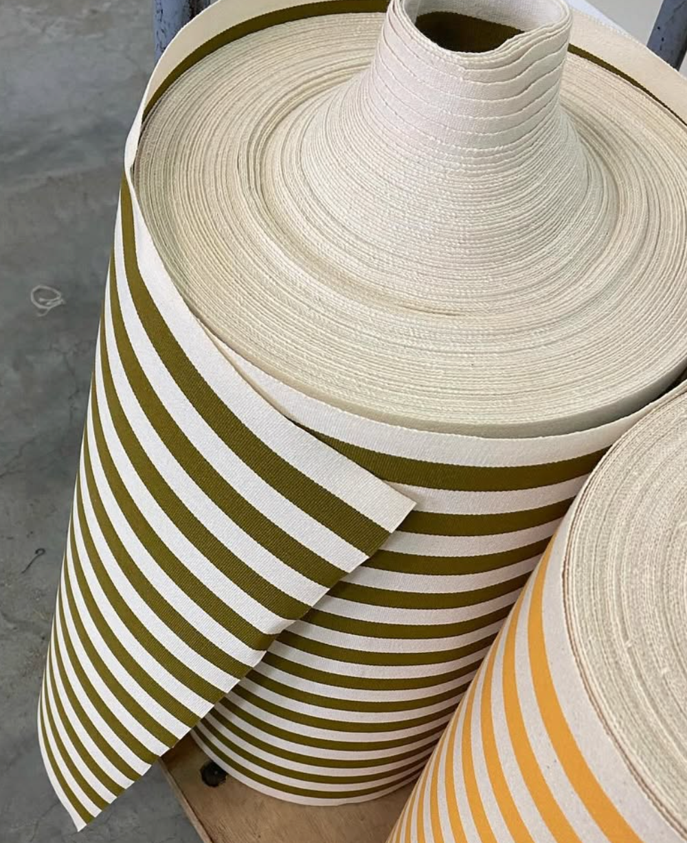 Rolls of fabric. One with ecru/natural and bronze/khaki stripes, and another yellow and ecru