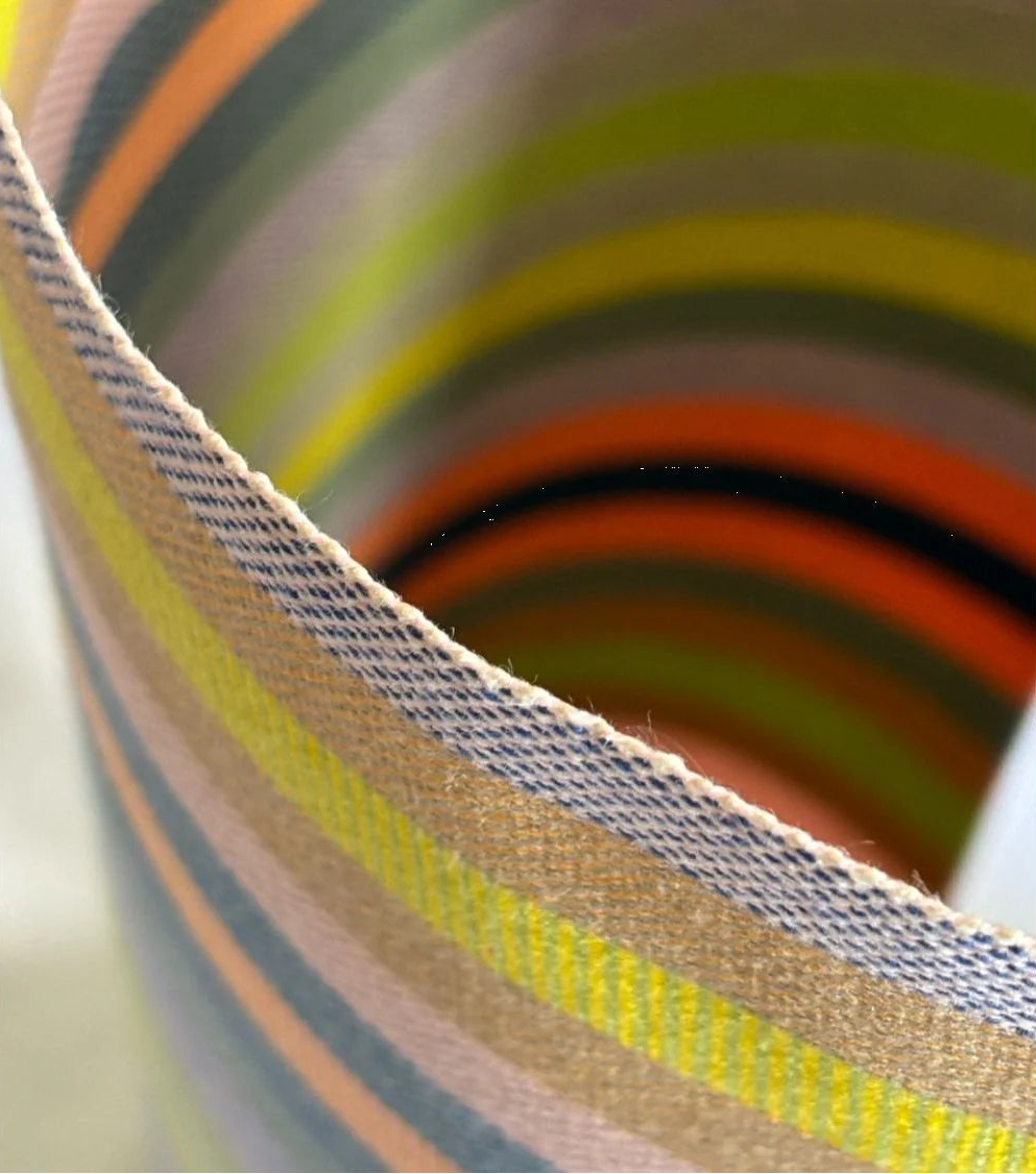Close up of colourful striped fabric roll on a white background. Showcasing orange, greens, blue, sage and other vibrant colours