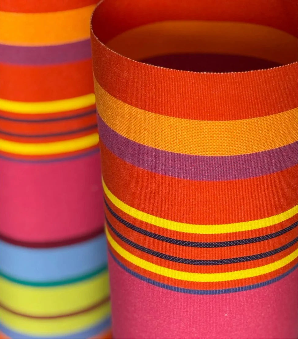 Close up of Bonbon Plume 43cm fabric featuring a striped pattern with vibrant stripes of orange, pink and red, punctuated with anise and fine bluish stripes. A detailed 100% cotton weave by By Les Toiles du Soleil