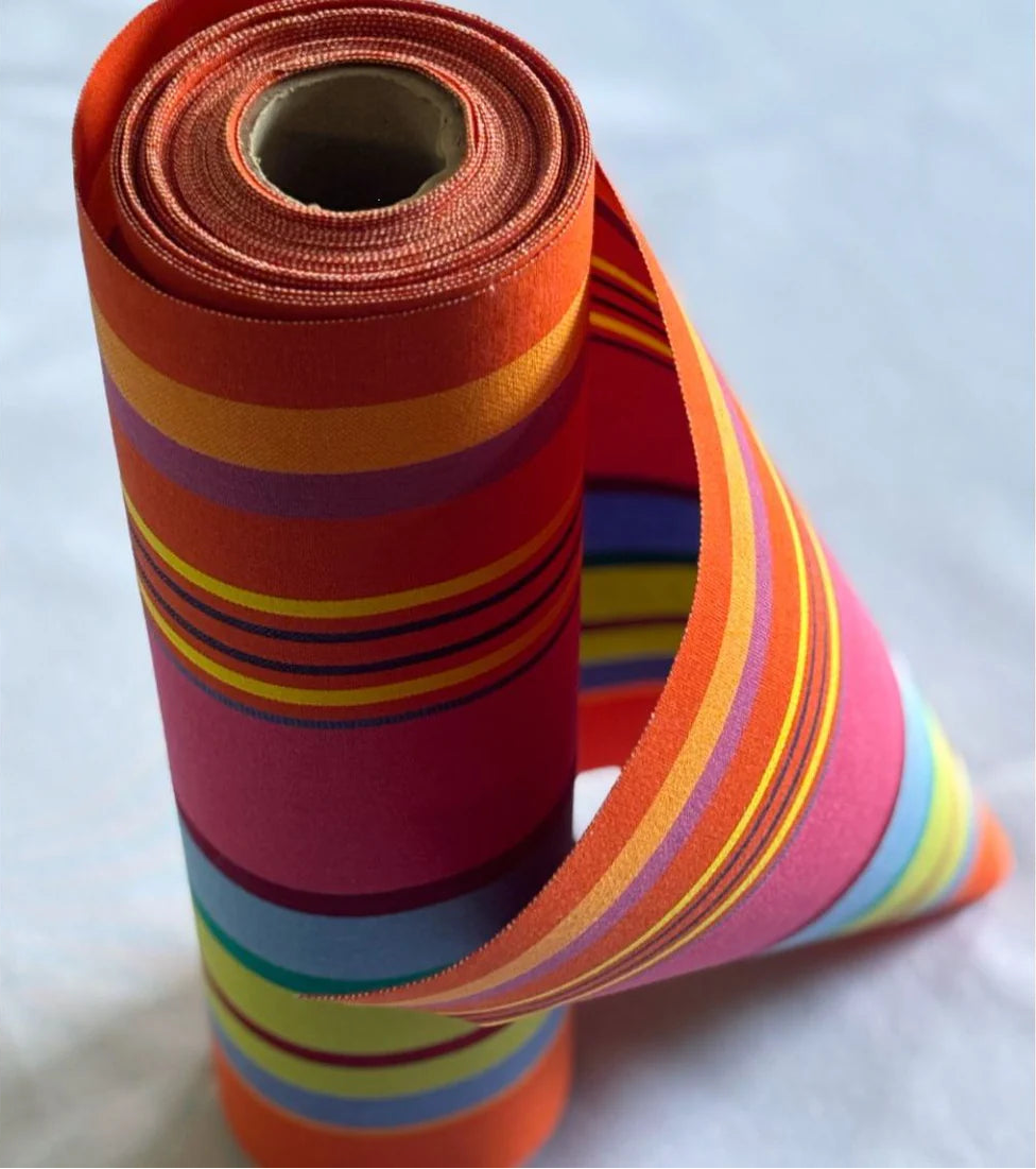 Roll of Bonbon Plume 43cm fabric featuring a striped pattern with vibrant stripes of orange, pink and red, punctuated with anise and fine bluish stripes. A detailed 100% cotton weave by By Les Toiles du Soleil