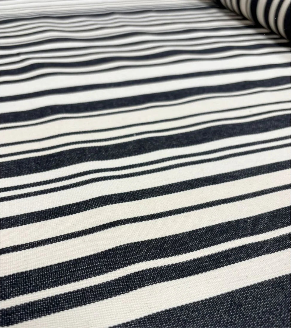 Close up of roll of 180cm cotton fabric by Les Toiles du Soleil called Tom Black. A multi striped pattern of white and black - like a barcode