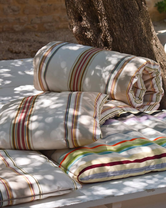 Stack of striped Les Toiles du Soleil custom pillows on a table outdoors with a tree in the background