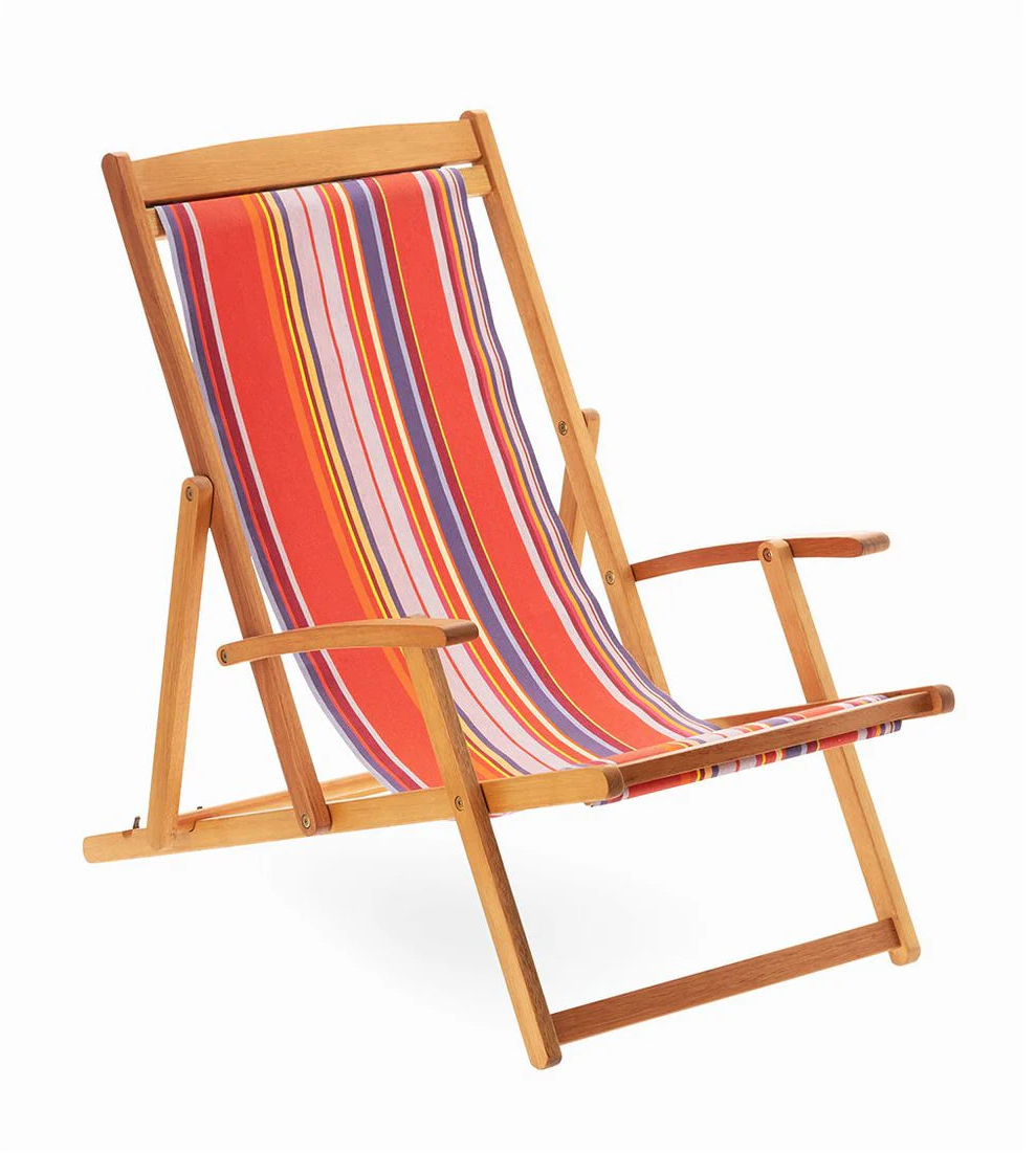 Wooden deckchair with colourful multi-striped cotton fabric. Showcasing vibrant pinks, lavender, purple, yellow, and orange. Petit Sixtine is a fabric made by Les Toiles do Soleil. White background