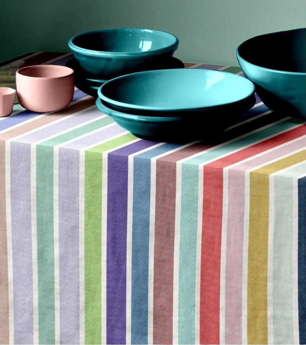 Tablecloth of 100% cotton Les Toies du Soleil fabric. The Èze range, made up of multi striped soft pastels, blues, purples, mint green, and other joyous colours. On top of the table cloth is pink and blue bowls