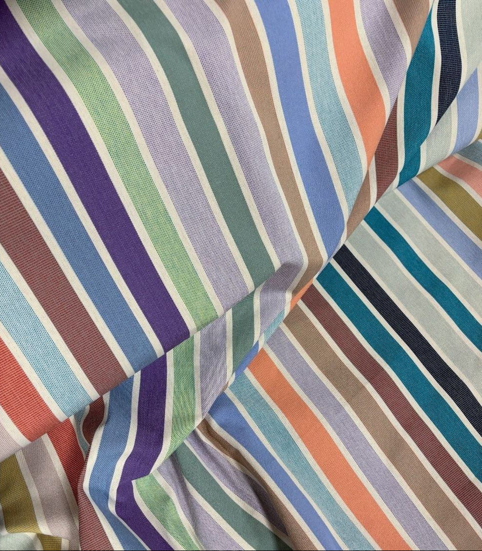 Close up of 100% cotton fabric roll of Èze. Showing the woven texture and multi striped colours of soft pastels, blues, purples, mint green, and other joyous colours