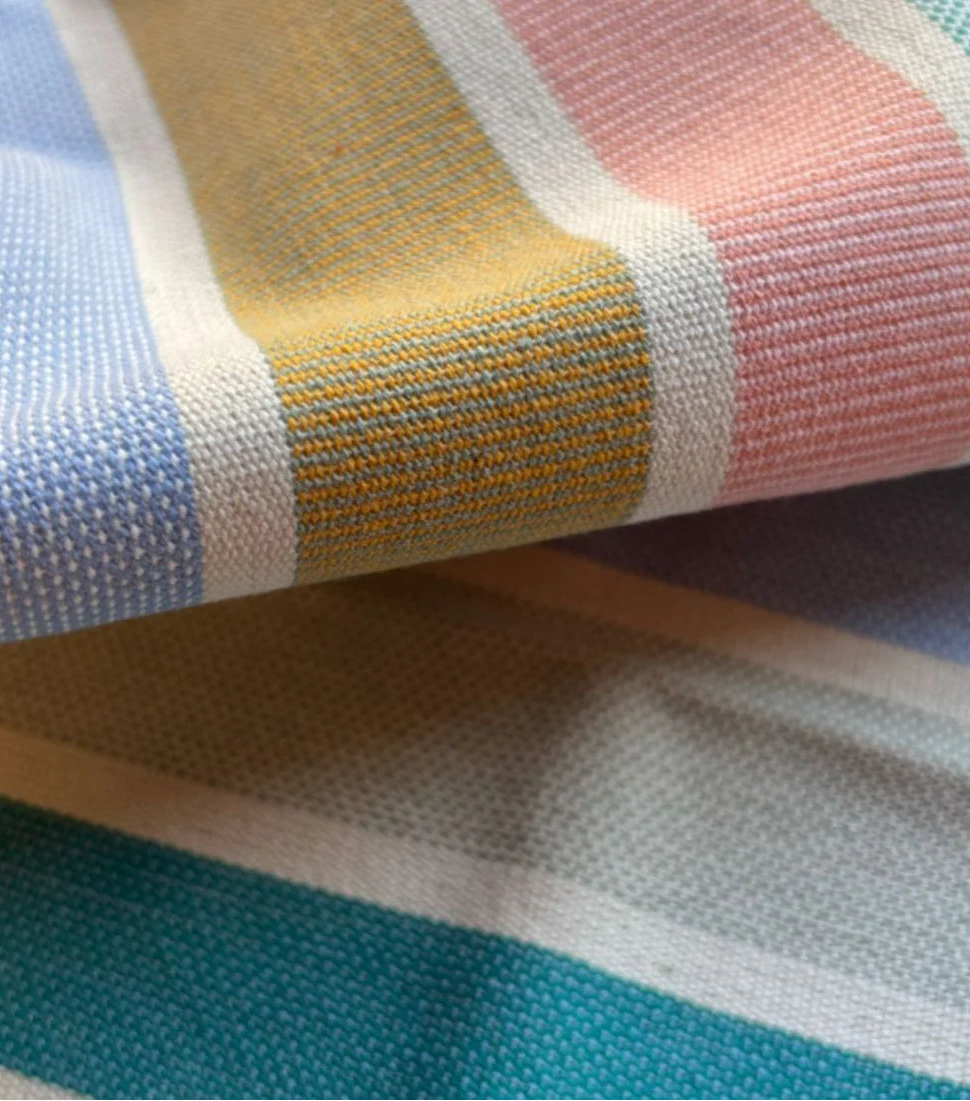 Close up of 100% cotton fabric roll of Èze. Showing the woven texture and multi striped colours of soft pastels, blues, purples, mint green, and other joyous colours