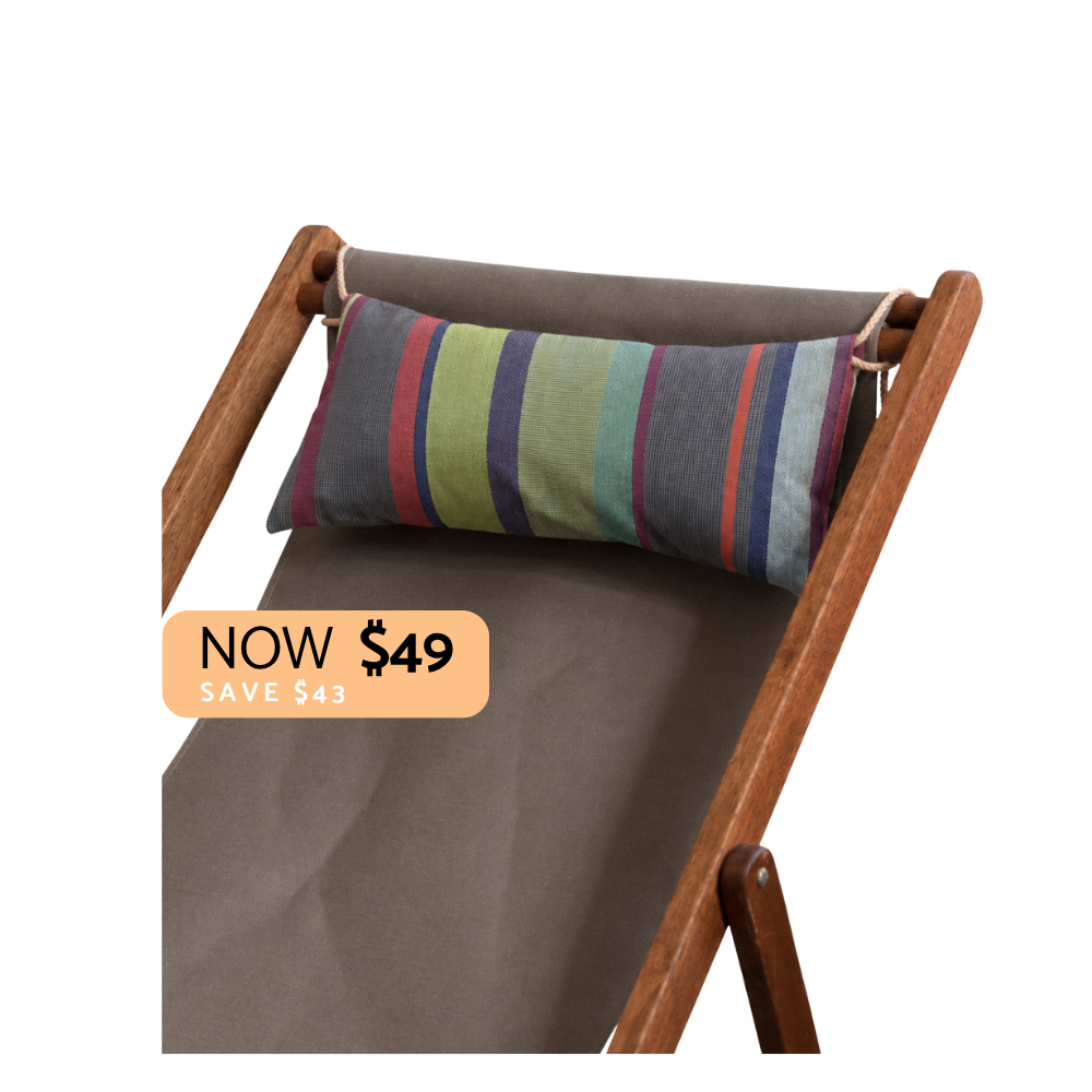 A striped lumbar pillow in muted green, blue, purple, and red tones, resting on the backrest of a brown wooden folding lounge chair with taupe fabric. A peach promotional badge reading 'NOW $49 SAVE $43' is overlaid on the lower left.