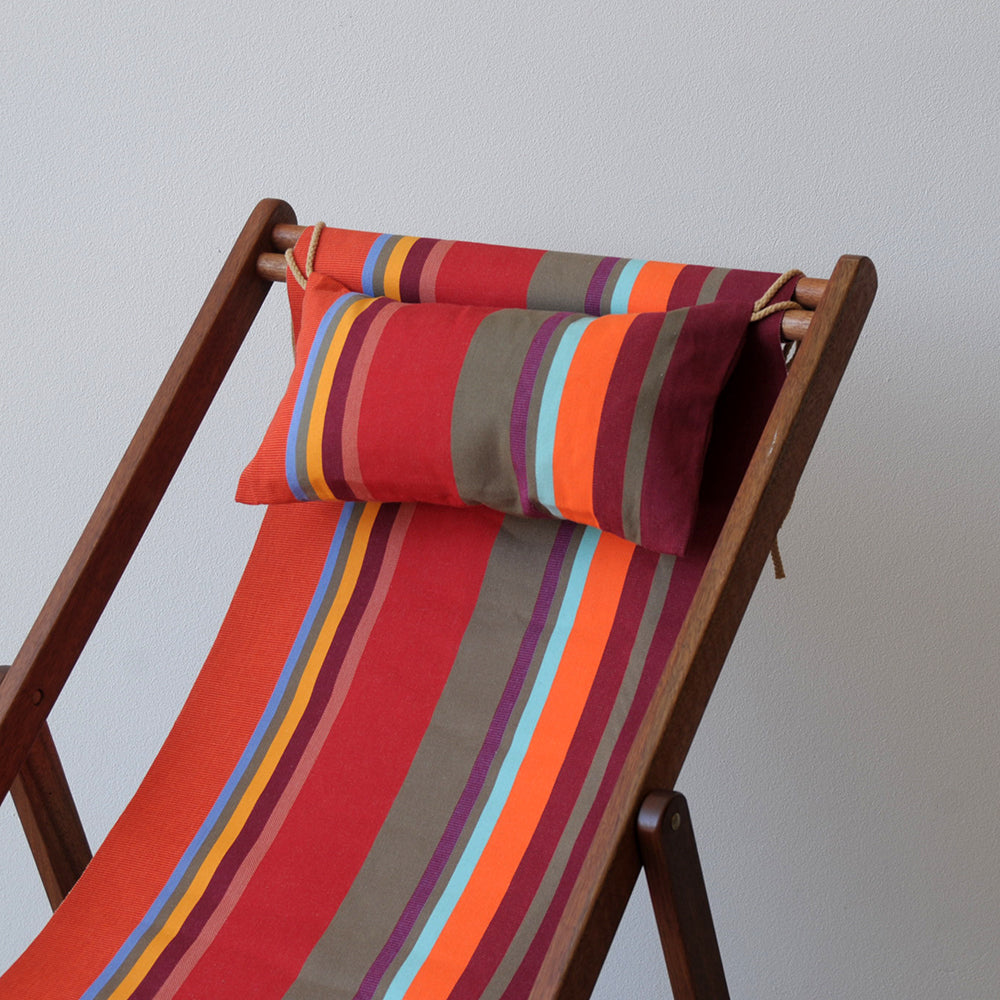 Ici et la deckchair and head pillow made from Collioure Rouge - a fabric featuring a striped pattern with various bands in reds, orange, taupe, burgundy, turquoise, and other vibrant colours. A detailed 100% cotton weave by By Les Toiles du Soleil