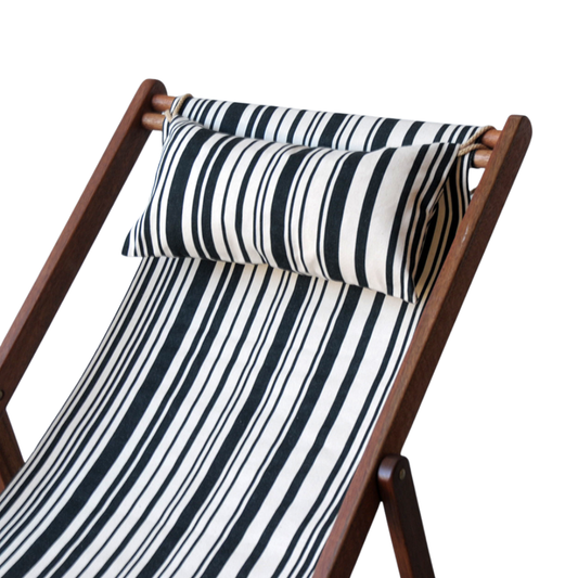 A black and white striped head cushion on a wooden deckchair frame, against a white wall.