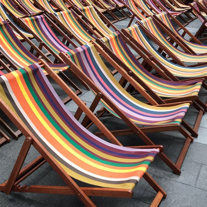 Row of colourful Les Toiles du Soleil striped deck chairs on a pavement