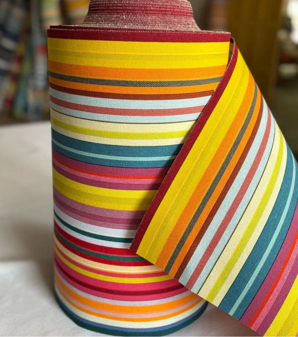 Spool of colourful striped fabric. Featuring thin strips of yellow, purple, blue, orange and other vibrant colours
