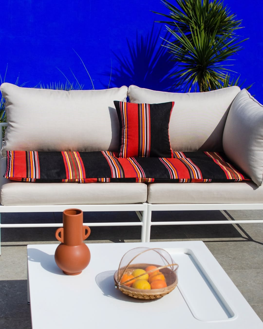 Outdoor setting with grey couch and bright blue background. The Outdoor couch is dressed with cushions and mattress by Les Touiles du Soleil, Jules Sunbrella fabric