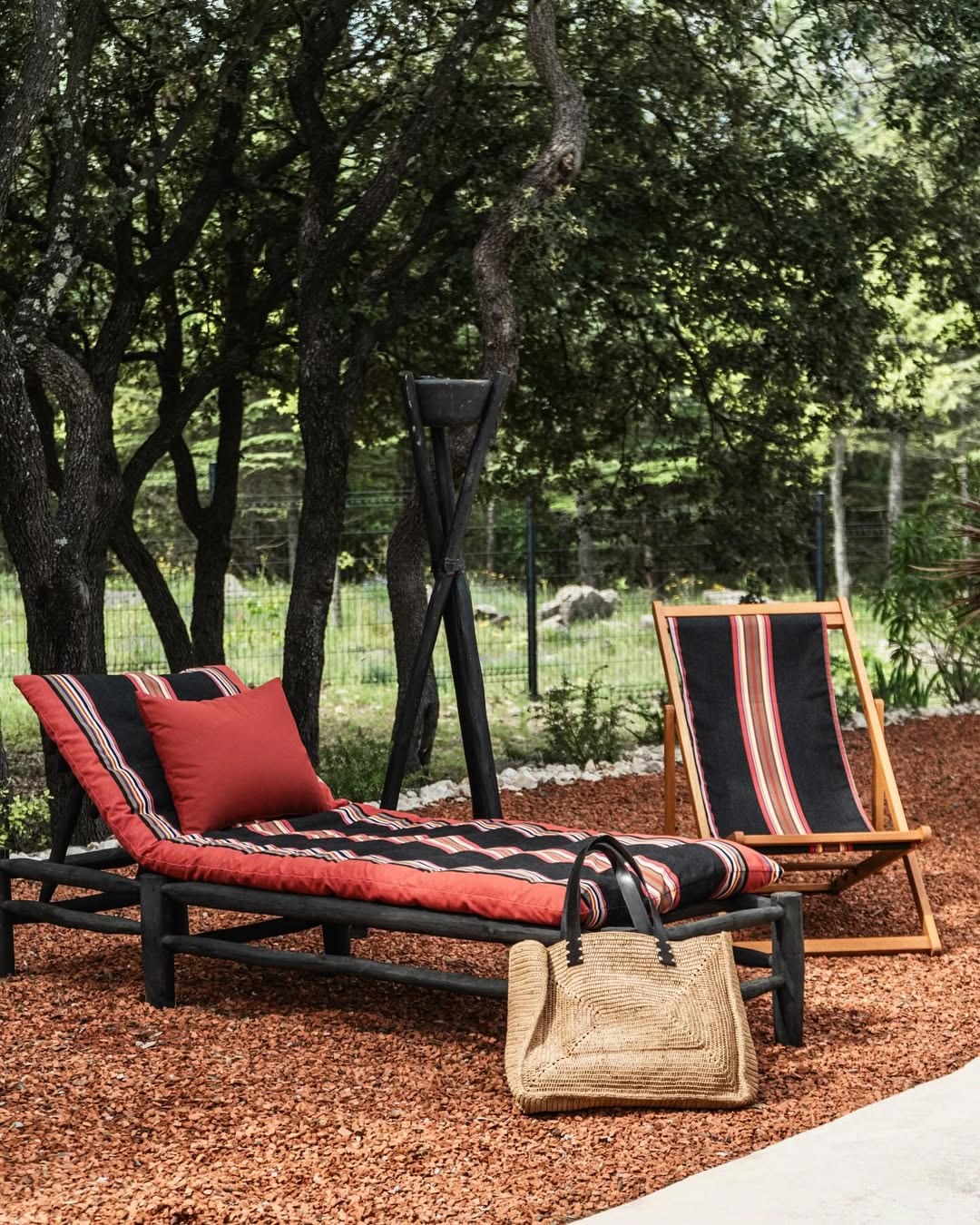 Out door setting with an sun lounger and deckchair on bark with trees in background. The furniture is made from the Jules fabric from Les Toiles du soleil, a Sunbrella outdoor fabric of black and warm multi striped colours