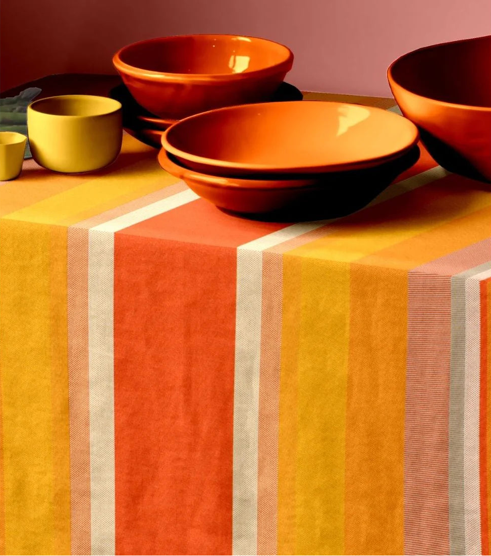 L'Apricot 100% cotton fabric table cloth by Les Toiles du Soleil. Warm coloured textured woven striped fabric with orange and yellow ceramic bowls placed on top.