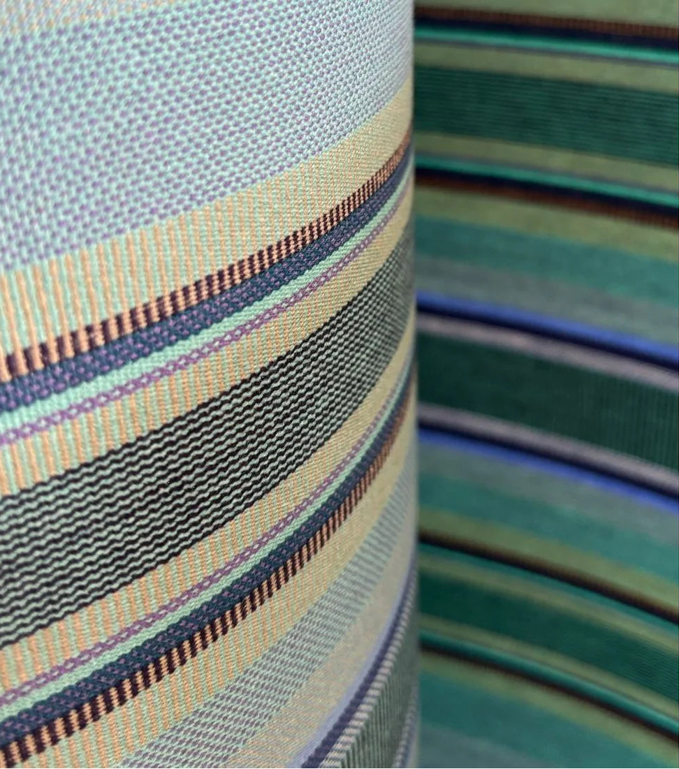 Close up of multi-coloured striped cotton fabric roll. Featuring a variety of blues, turquoise, and shades of greens with a detailed weave. 