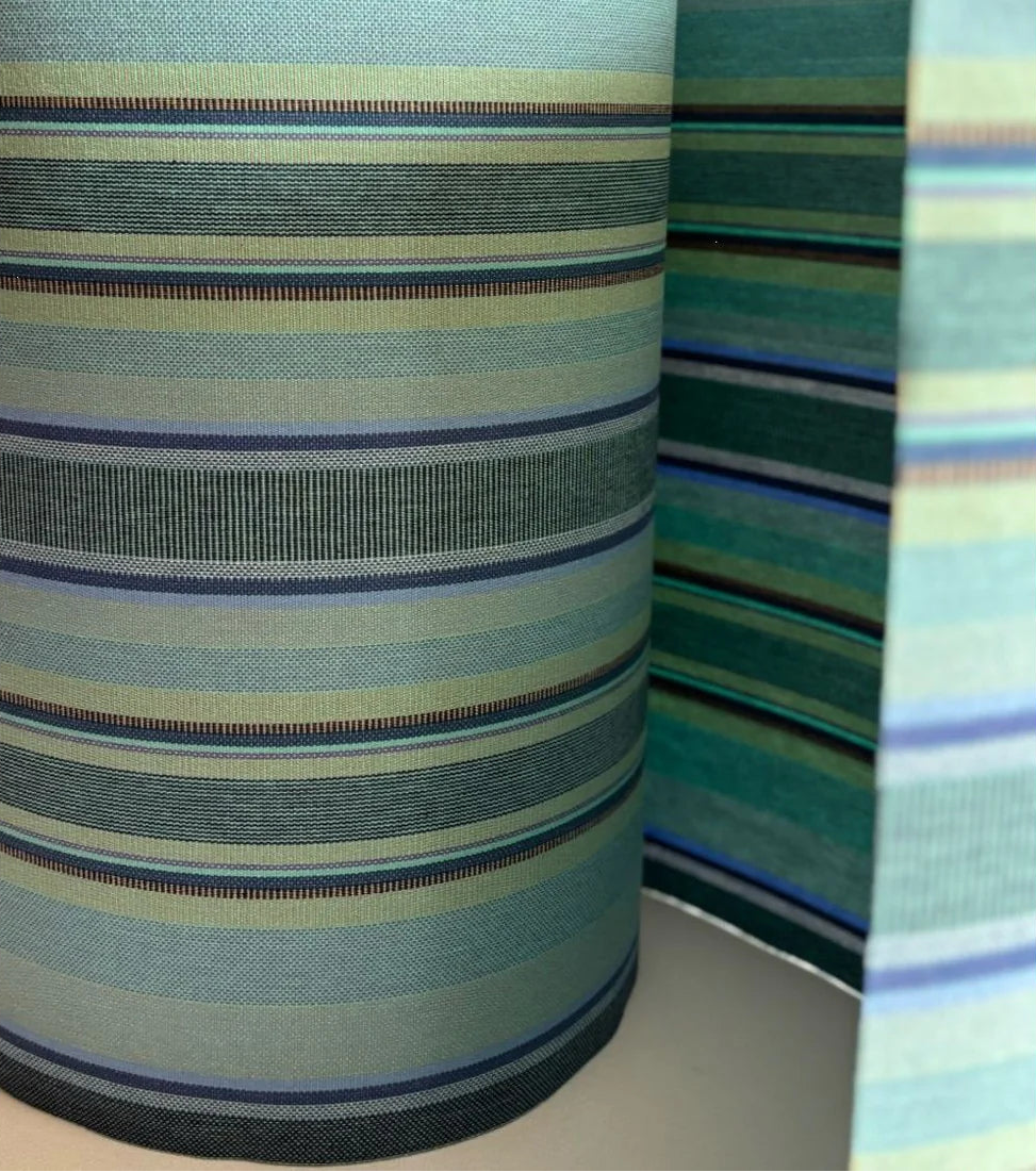 Multi-coloured striped cotton fabric roll. Featuring a variety of blues, turquoise, and shades of greens with a detailed weave. 