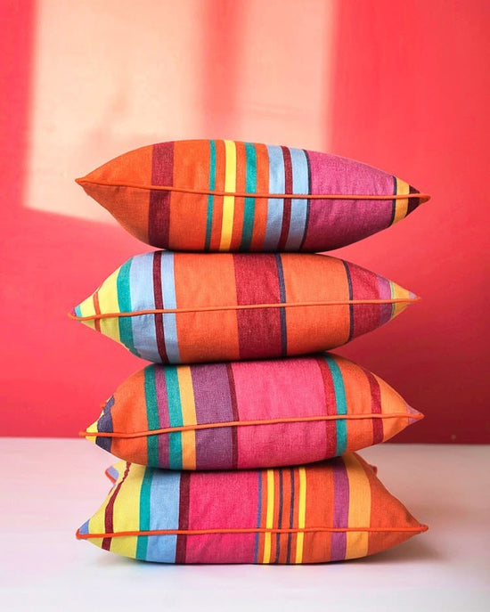 Stack of coloruful Ls Toiles du Soleil 100% cotton striped pillows against a red background