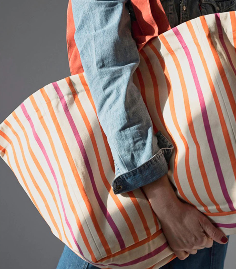 Body shot of a women carrying a large shoulder bag made from vibrant thin sailor stripes of orange and fuchsia on a 43cm 100% cotton fabric called Marin Orange by Les Toiles du Soleil.