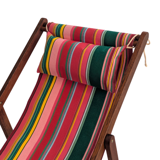A hardwood folding deck chair with a colourful striped fabric sling and matching striped headrest pillow, featuring stripes of red, purplish crimson, candy pink, green, blue and golden yellow, inspired by the colours of the Catalan town of Toulouges and its famous onion.shown on a plain white background.