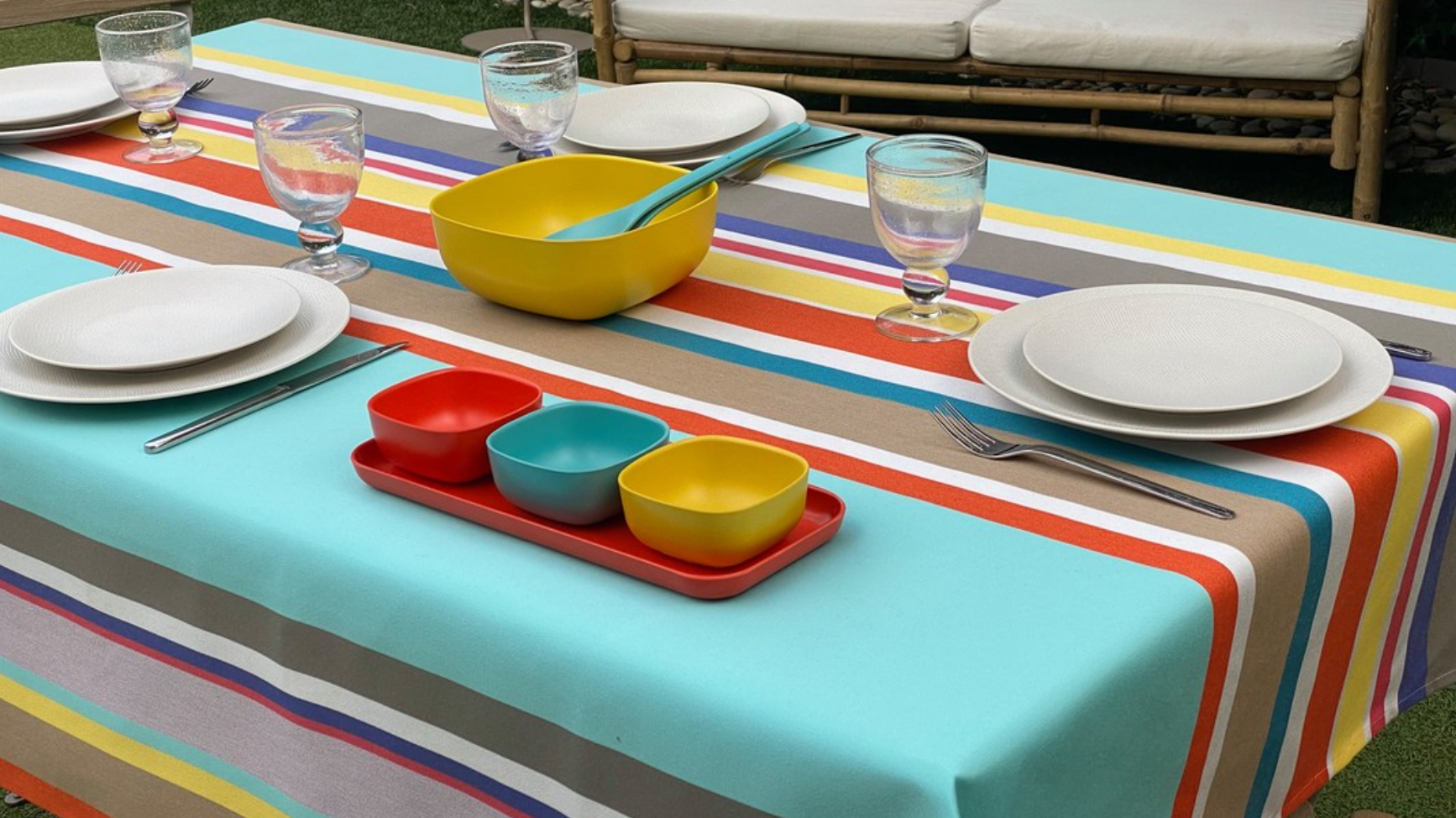 Colorful striped Parasol Outdoor Fabric tablecloth with plates, bowls, and glasses on a table.