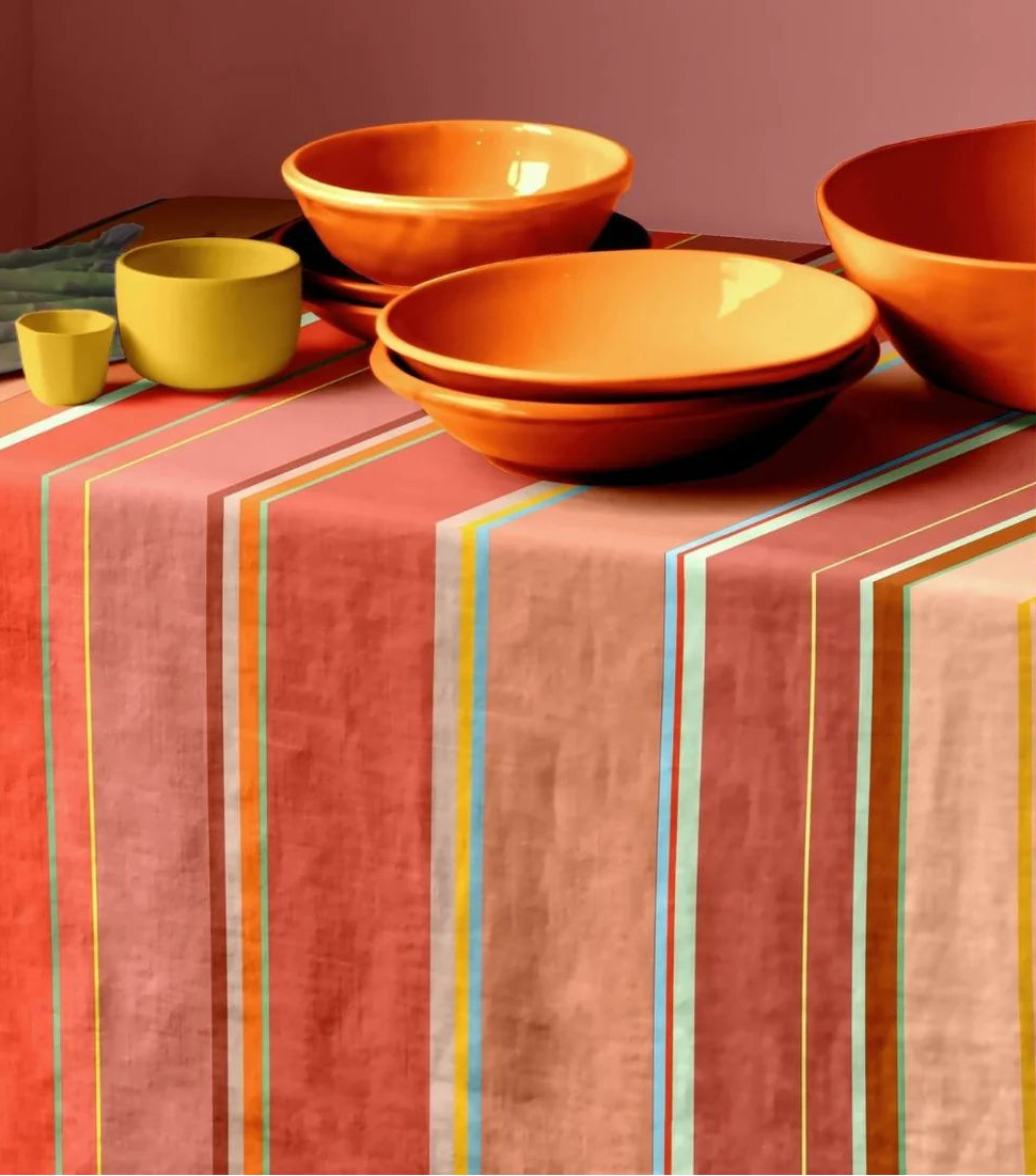 Colorful table setting with orange bowls on a striped tablecloth by Les Toiles du Soleil 100% cotton Pezilla-la-rivière fabric. Striped with Multi colours - ight stone and terracotta, soft greens, subtle rusts and the patinated reds.