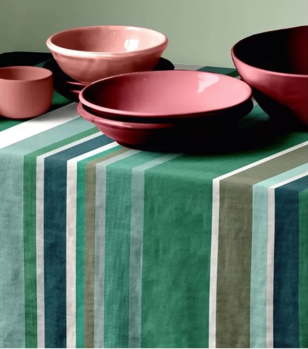 Dining table setting with a tablcloth mafe from Place aux Herbes - a 100% cotton fabric roll which is a vibrant striped tapestry: fresh greens, almond, olive and taupe. The setting has several rose coloured ceramic bowls on top