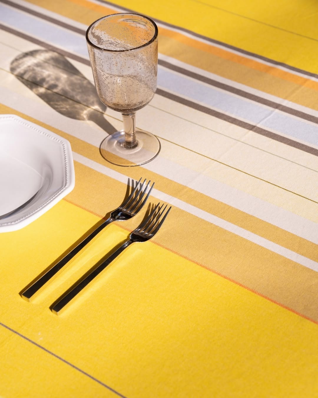 Table setting with Close up of Plein Soleil multi coloured yellow, grey, and sun toned striped Les Toiles du Soleil 100% cotton fabric. 