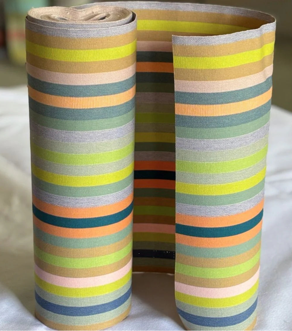Colourful striped fabric roll on a white background. Showcasing orange, greens, blue, sage and other vibrant colours