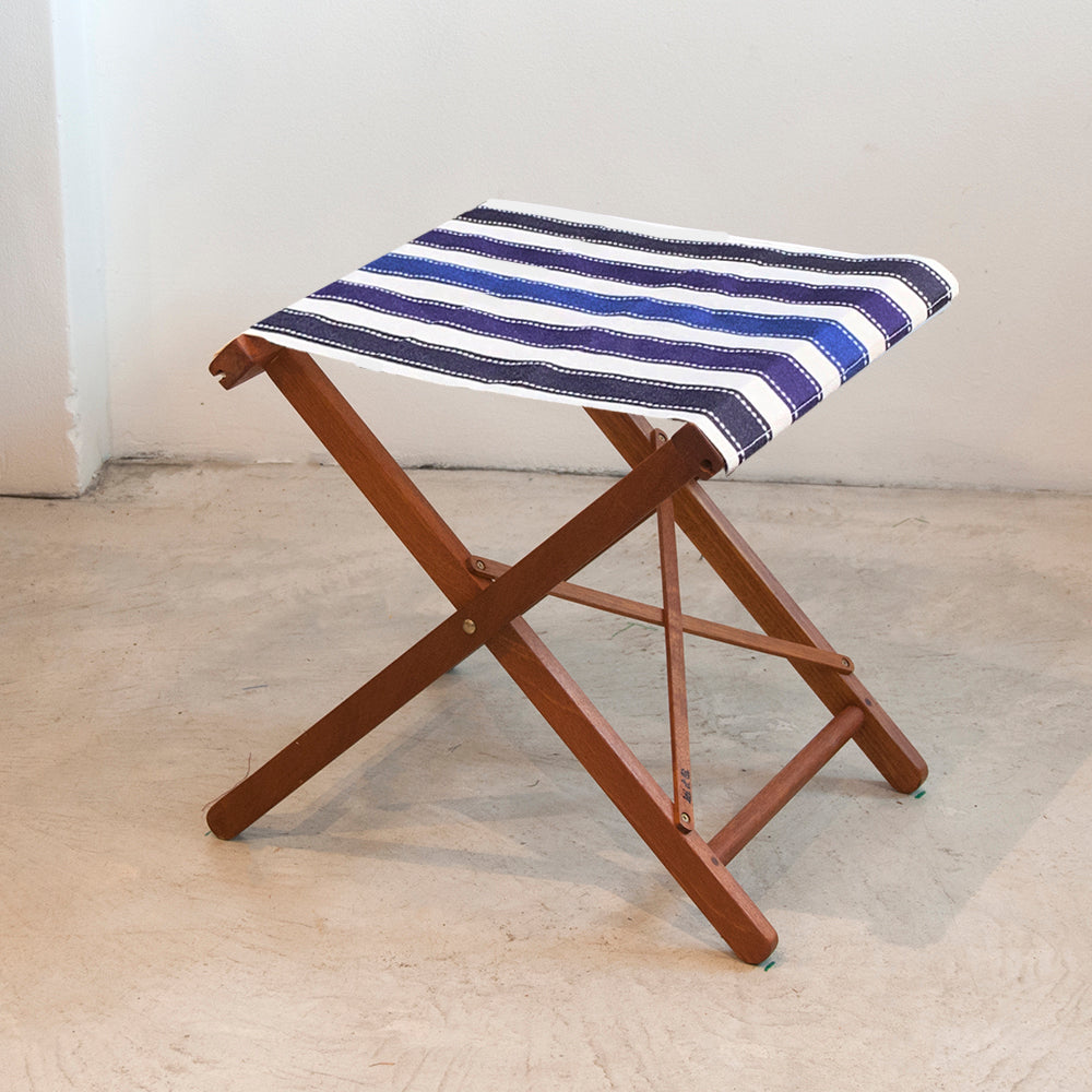 ici et la folding stool made from Petit Sellier. A fabric featuring a striped pattern with various bands in different shades of blue. A detailed 100% cotton weave by by Les Toiles du Soleil