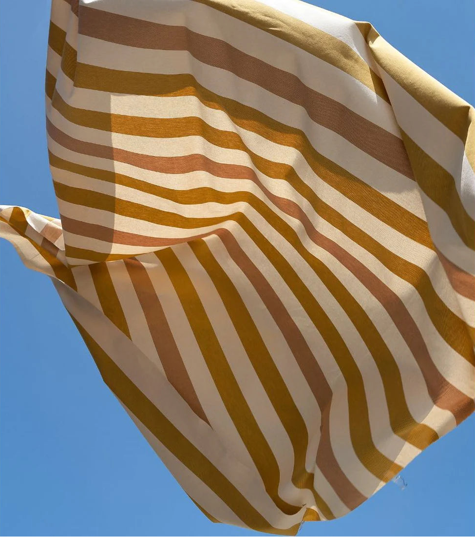 Raspail Miel Les Toiles du Soleil 100% cotton yellow, white and muted pink stripes fabric thrown in the air with a blue background